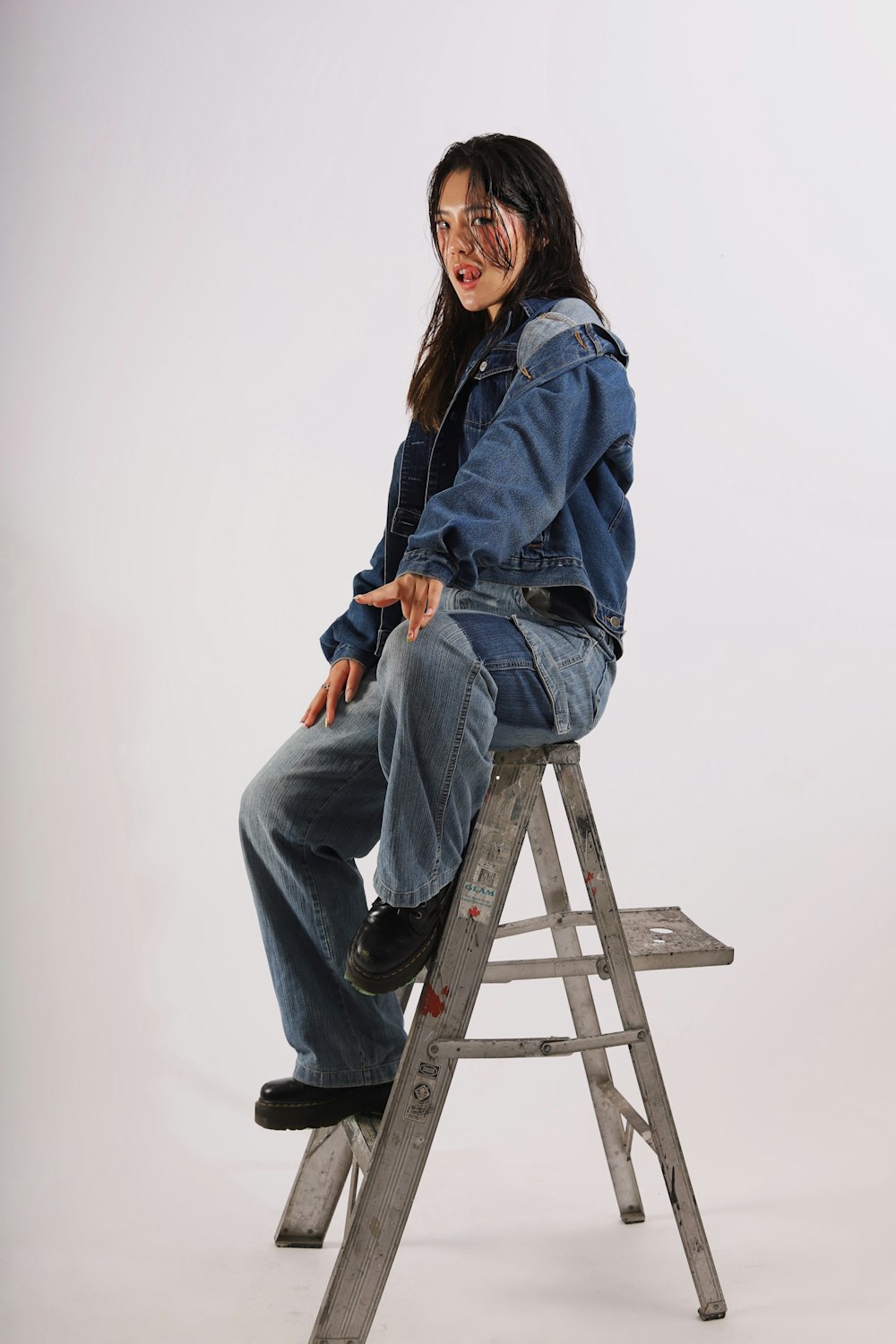 woman in blue denim jacket and blue denim jeans sitting on brown wooden seat