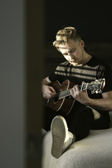 A candid photo of Mariah Kronvik playing an acoustic guitar under soft, natural light with her eyes closed, lost in the music.