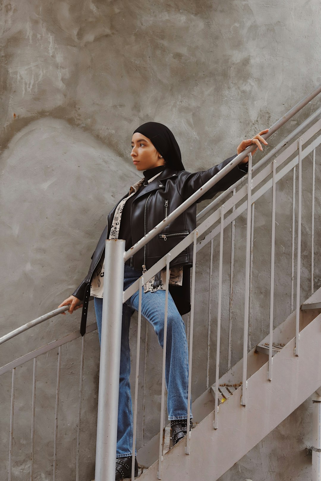 woman in black hijab and blue denim jeans sitting on white metal railings
