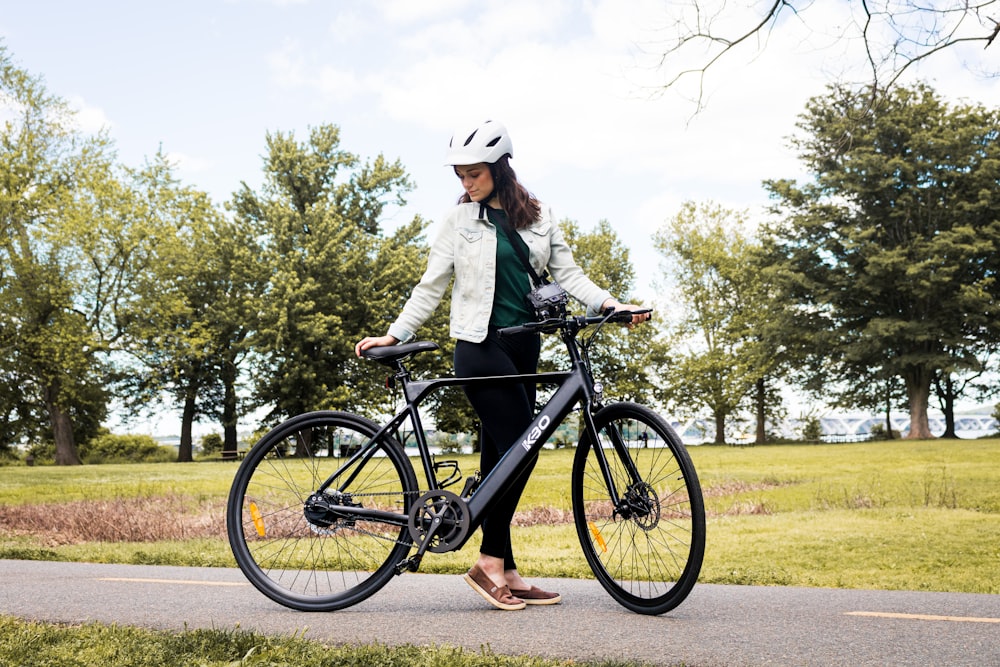 woman in gray coat riding black mountain bike on green grass field during daytime