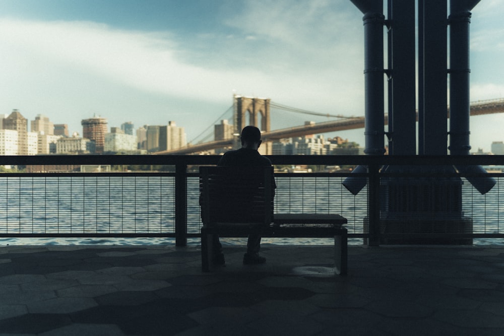 man sitting on bench near body of water during daytime