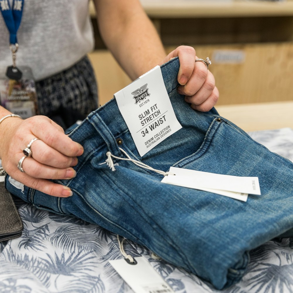 Persona en jeans de mezclilla azul sosteniendo papel blanco