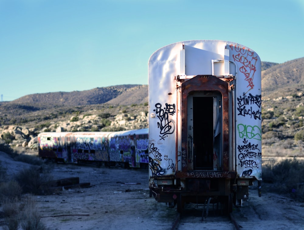 a train covered in graffiti sitting in the middle of a desert