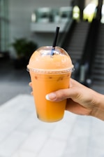 person holding orange juice in clear plastic cup