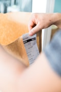 A person's hand is holding a brown paper bag which contains a receipt with the Uber Eats logo. The receipt indicates a delivery order with items listed such as iced lattes and contains delivery details.