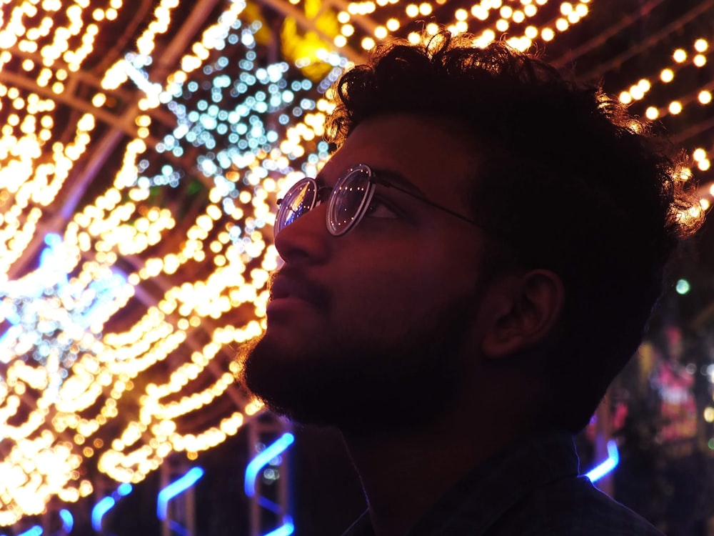 a man with glasses standing in front of christmas lights
