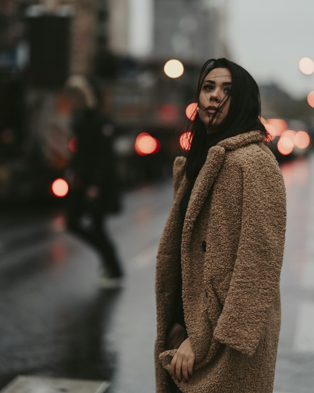 woman in brown coat standing on street during night time