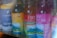 Several bottles of Sky Kombucha in various flavors are lined up in a refrigerator. The bottles have colorful labels with images of mountains and are placed next to a tall can of La Colombe Coffee Draft Latte made with oat milk.