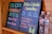 Two black chalkboards list drink options: one offers celery orange juice, and the other features a piña colada smoothie. Prices and sizes are displayed in vibrant colors. Two plastic water bottles sit beside the boards, partially visible.