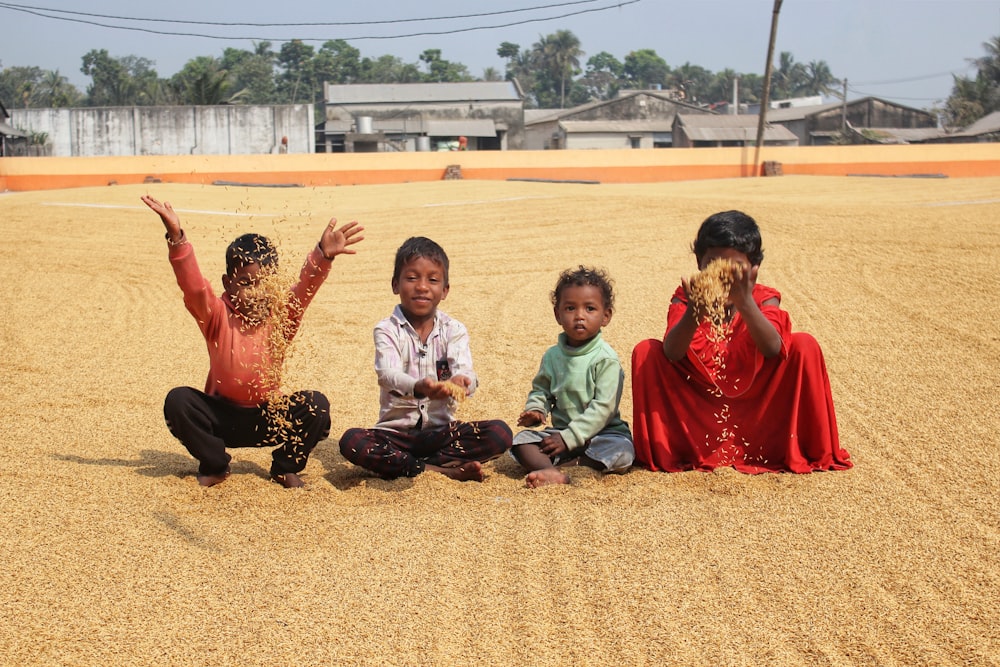 3 boys sitting on brown sand during daytime