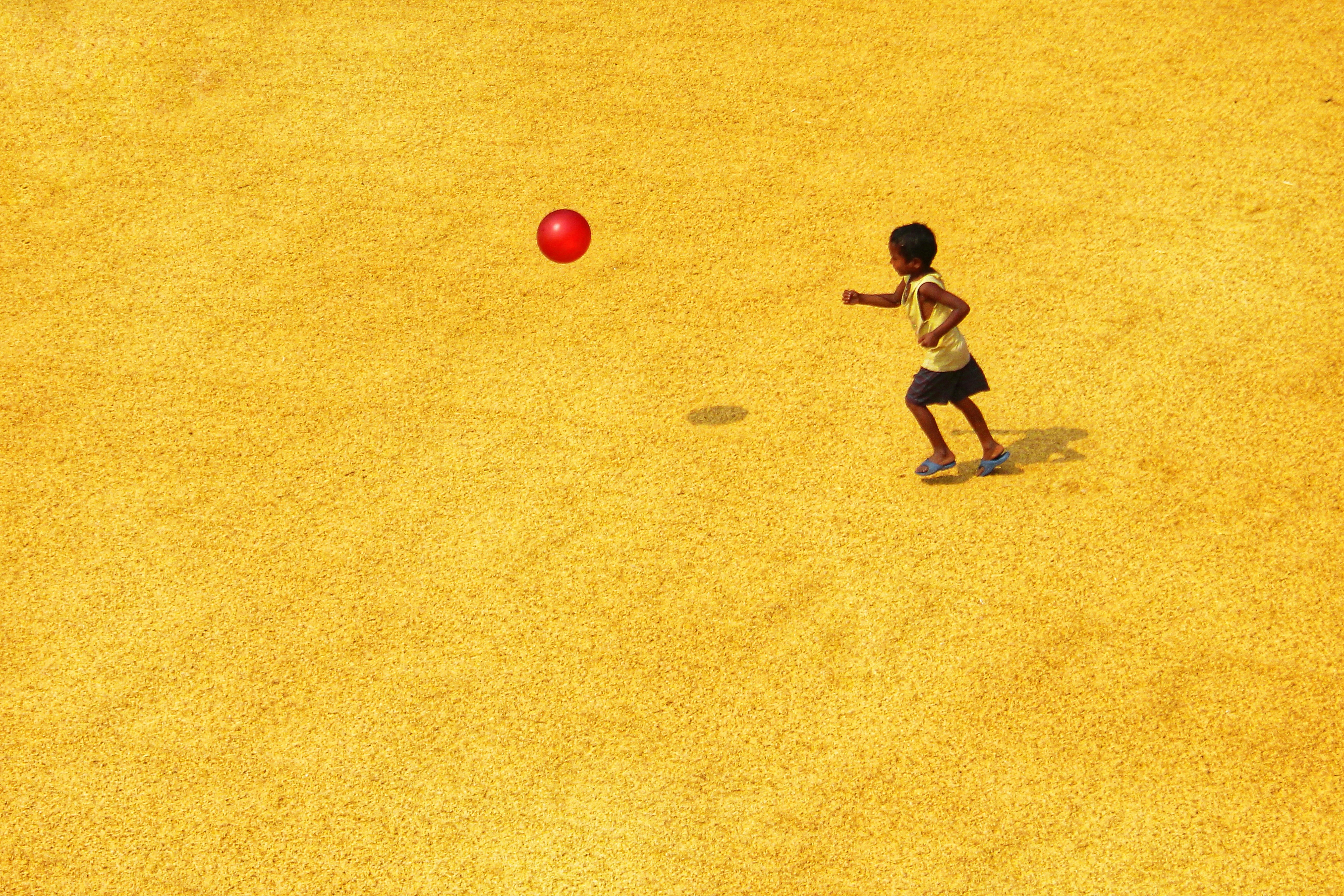 boy in black t-shirt playing with red ball on brown field