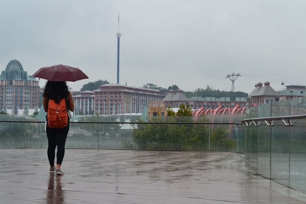 주황색 배낭을 멘 여자가 우산을 들고 빗속을 걷고 있다