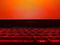 A laptop keyboard illuminated with a bright red backlight is in the foreground, while the screen displays a plain orange background. The brand name 'LEGION' is visible above the keyboard.
