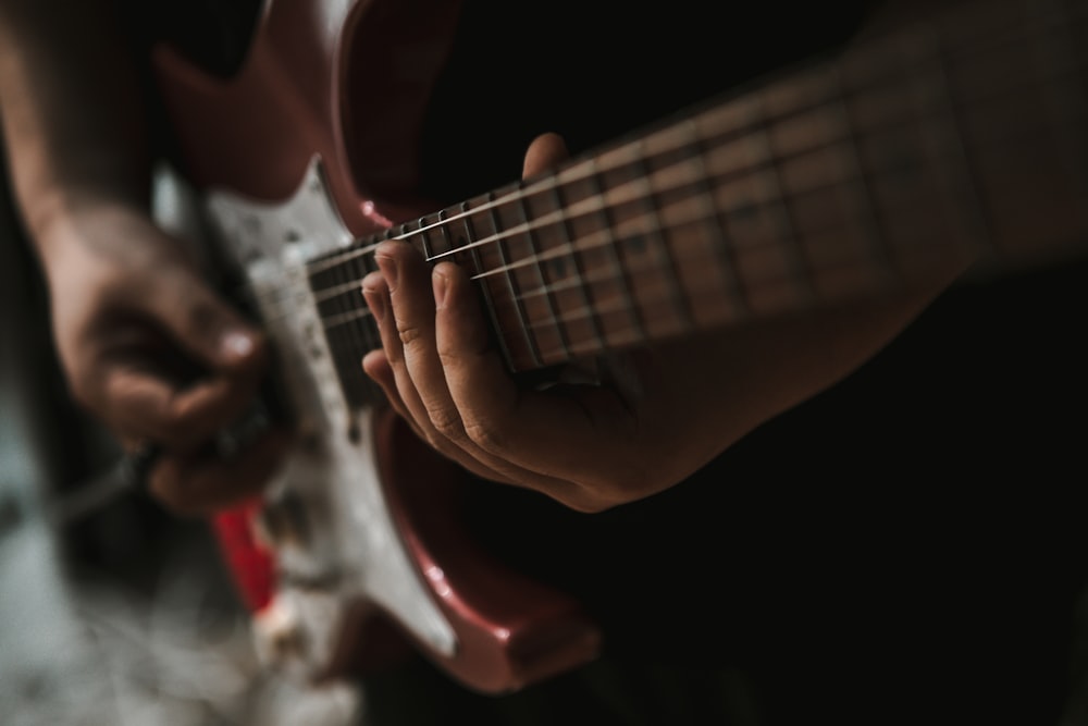 person playing red and white electric guitar