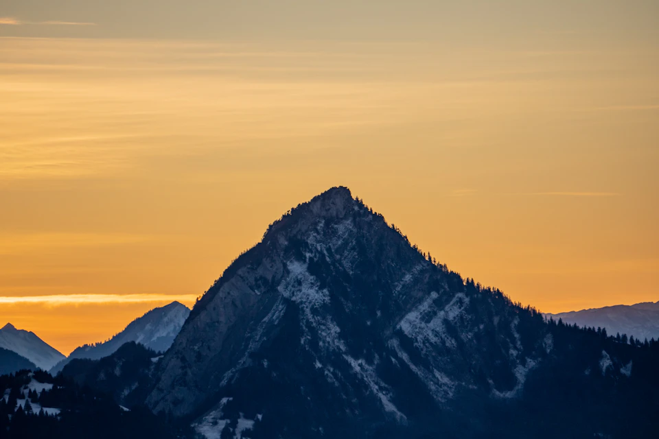 Majestic mountain range with snow-capped peak bathed in warm orange and yellow hues during sunset