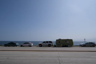 A lineup of different rental cars parked along a sunny coastal road.
