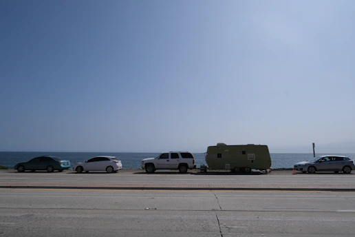 A lineup of different rental cars parked along a sunny coastal road.