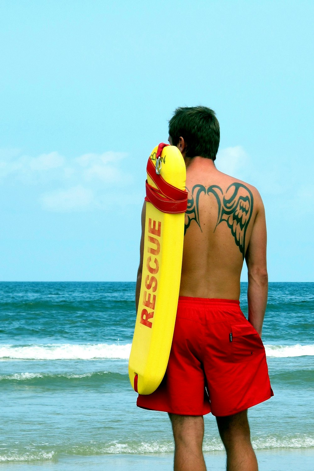 um homem de calção vermelho segurando uma prancha de surf amarela