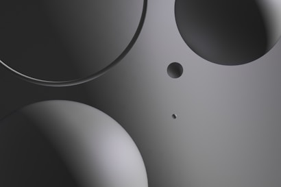 Various circular shapes in different sizes are positioned on a smooth, gradient background. The image primarily uses shades of gray, with a sleek and modern look.