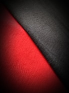 The image captures a close-up view of two fabrics side by side. One fabric is black, and the other is a vibrant red, with a noticeable texture visible on both surfaces. The light appears to create a soft gradient, enhancing the contrast between the two colors.