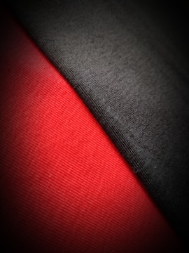 The image captures a close-up view of two fabrics side by side. One fabric is black, and the other is a vibrant red, with a noticeable texture visible on both surfaces. The light appears to create a soft gradient, enhancing the contrast between the two colors.