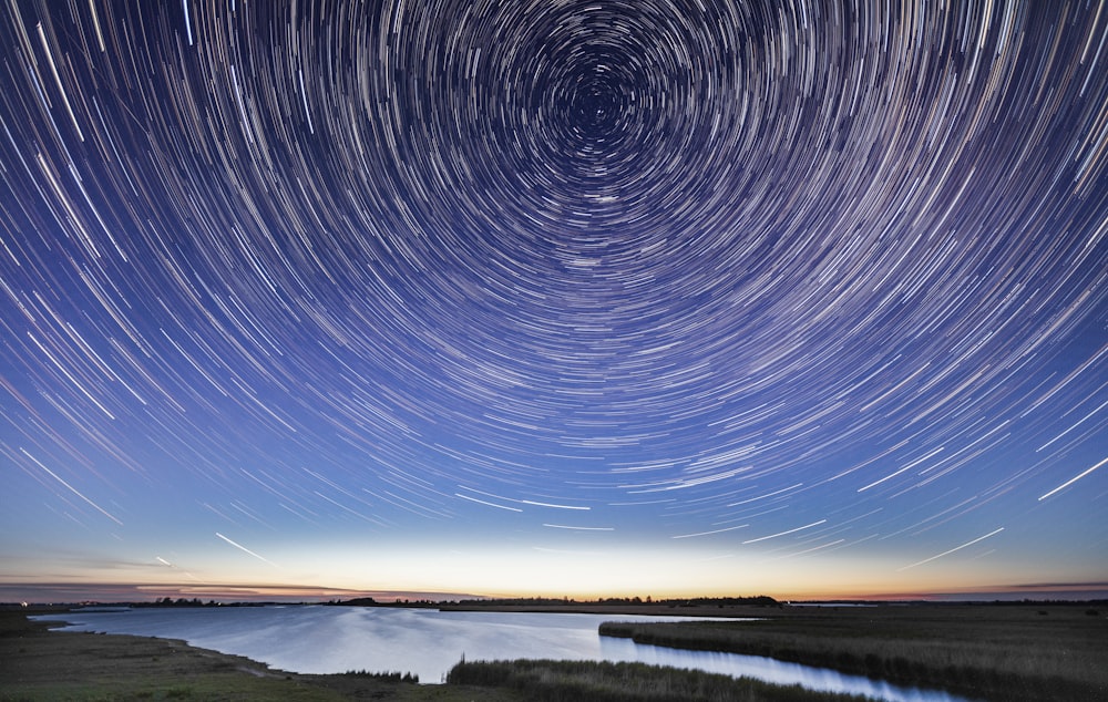 time lapse photography of stars above body of water during night time