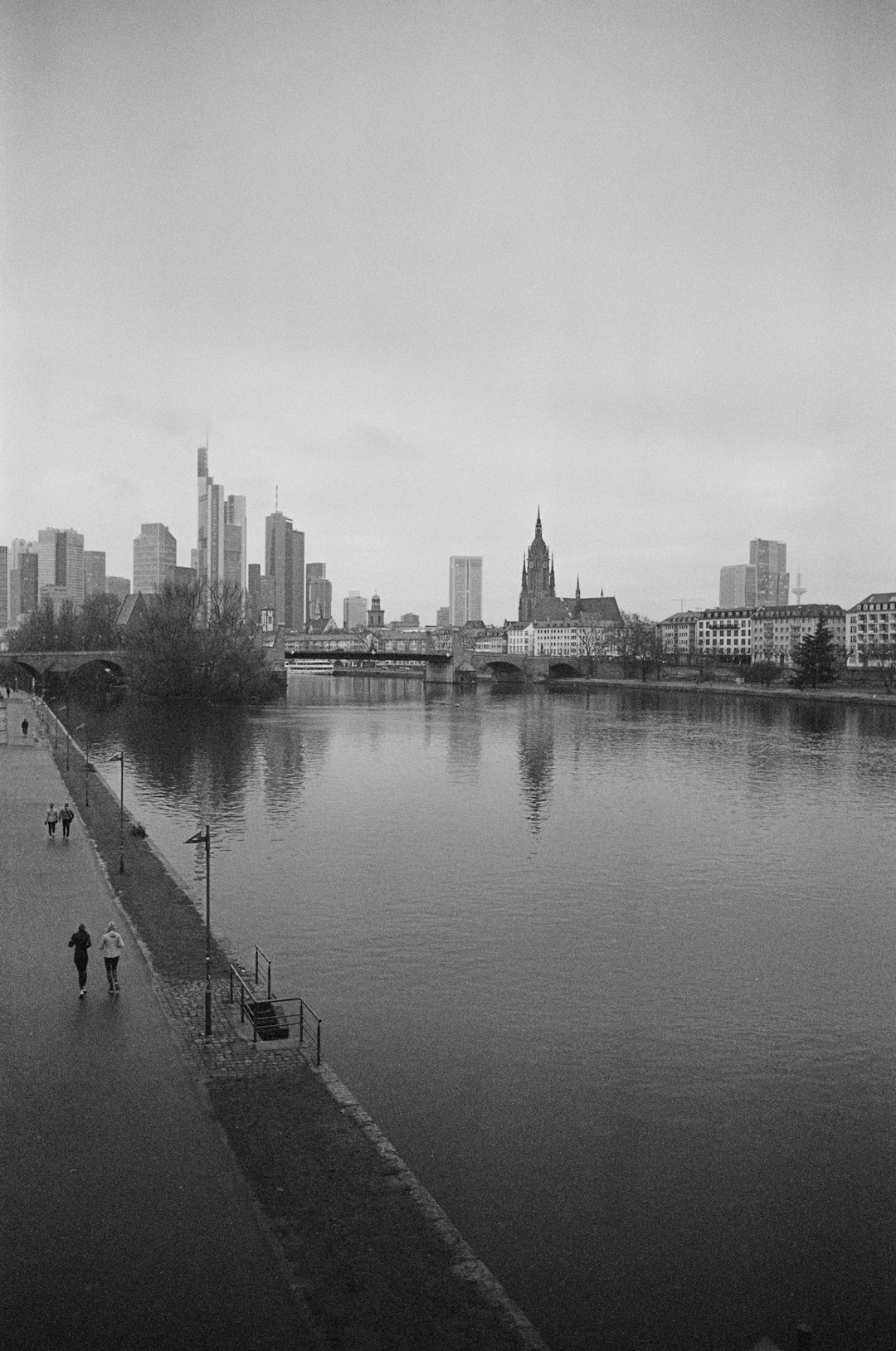 grayscale photo of people walking on sidewalk near body of water