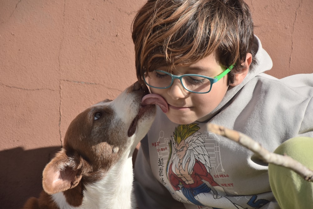 a boy in glasses kissing a dog on the nose