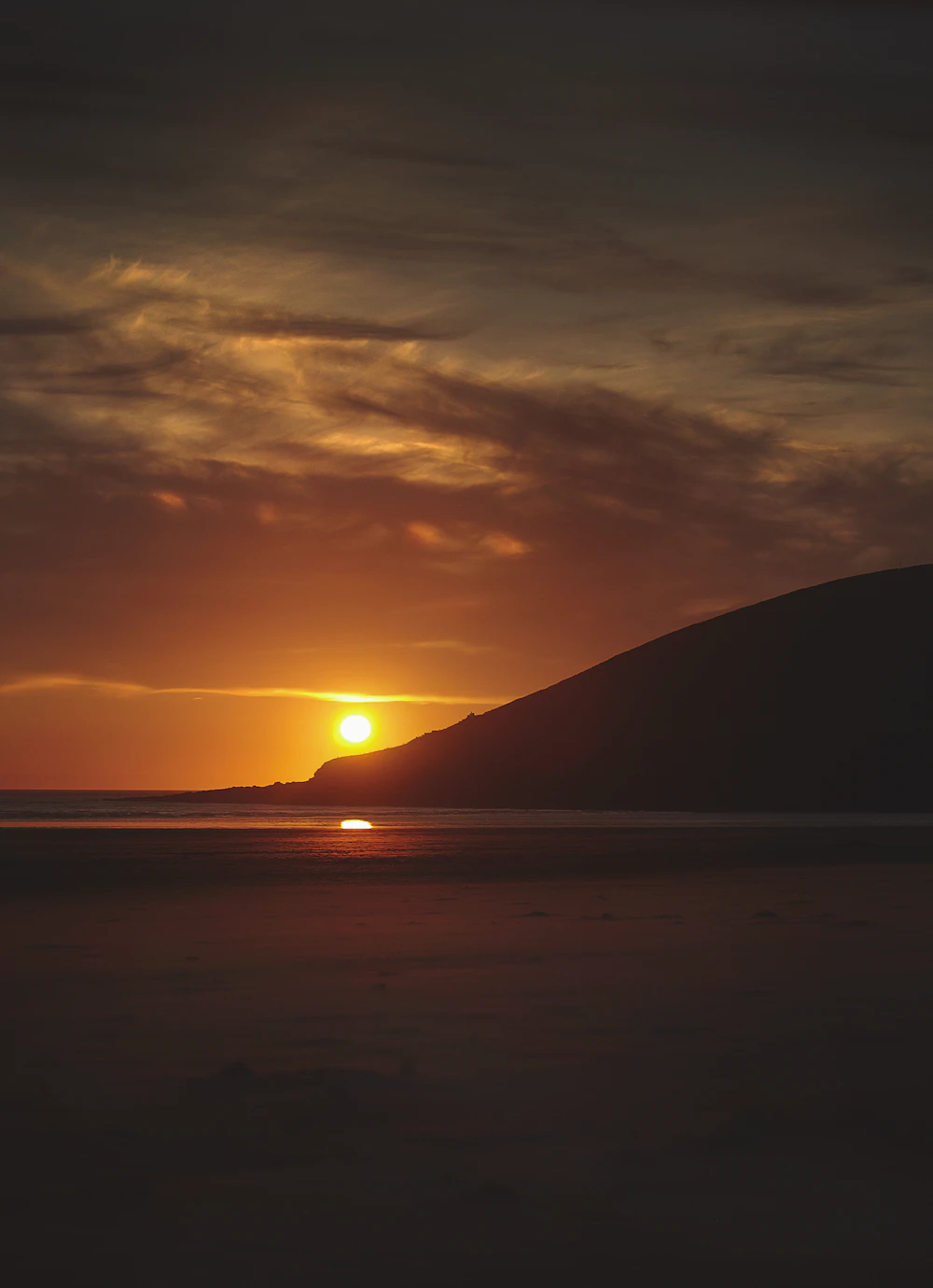 The sun setting over the sea beside a dark headland