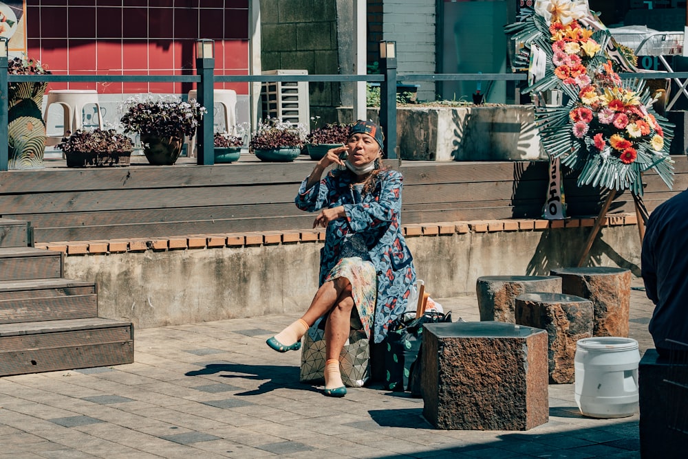 昼間、茶色のコンクリートのベンチに座っている黒と白の花柄のドレスを着た女性