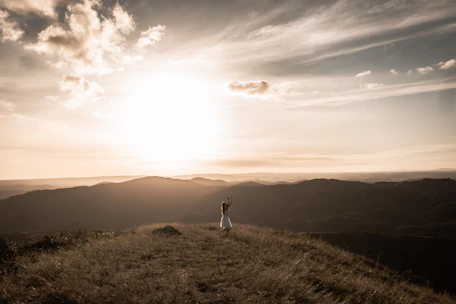 A person standing tall on a hilltop at sunrise, arms open wide embracing the new day.