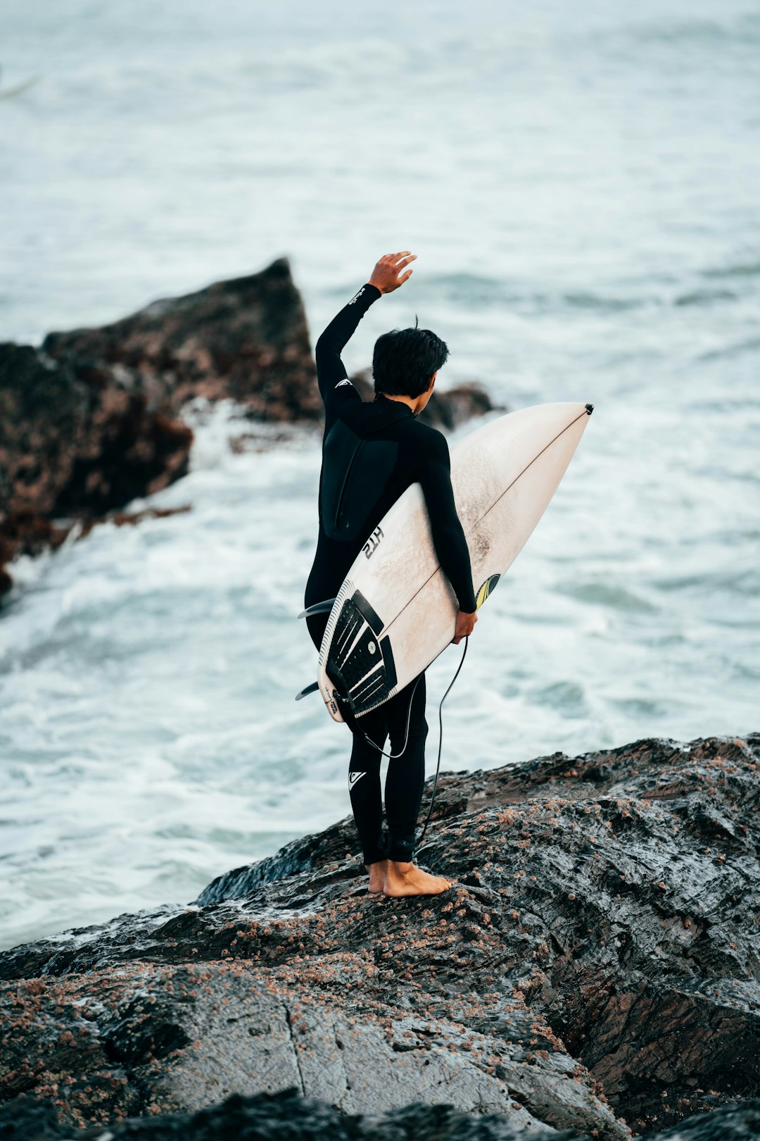 man in black long sleeve shirt carrying white surfboard standing on rocky shore during daytime