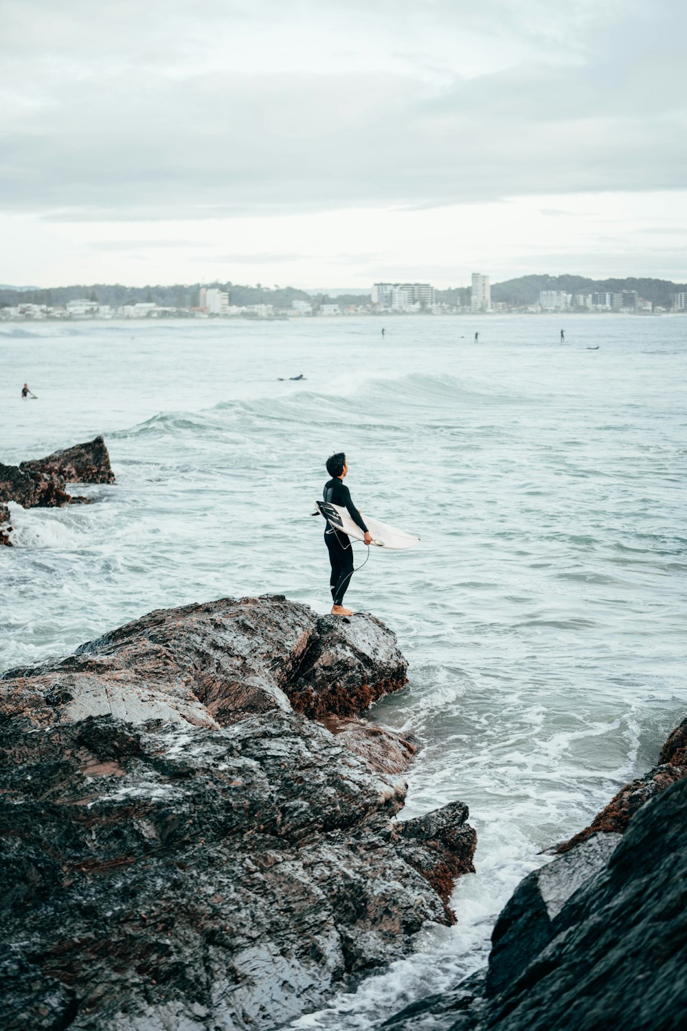 a person standing on a rock with a surfboard