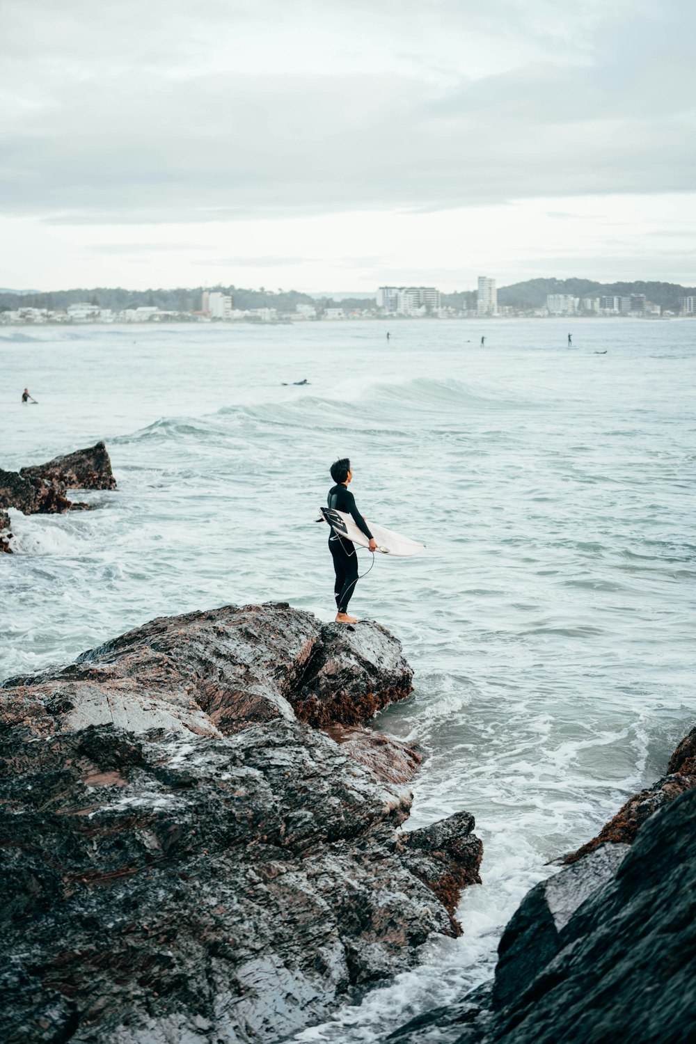una persona in piedi su una roccia con una tavola da surf