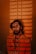 A man stands with a projection of the phrase 'Escape the Ordinary' repeatedly displayed across his face and body. The background appears dimly lit with a warm, reddish hue, creating a striking visual effect.