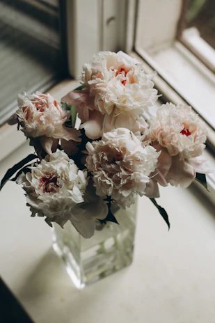 Delicate silk peonies in soft pink and cream tones displayed in a gold-trimmed glass vase