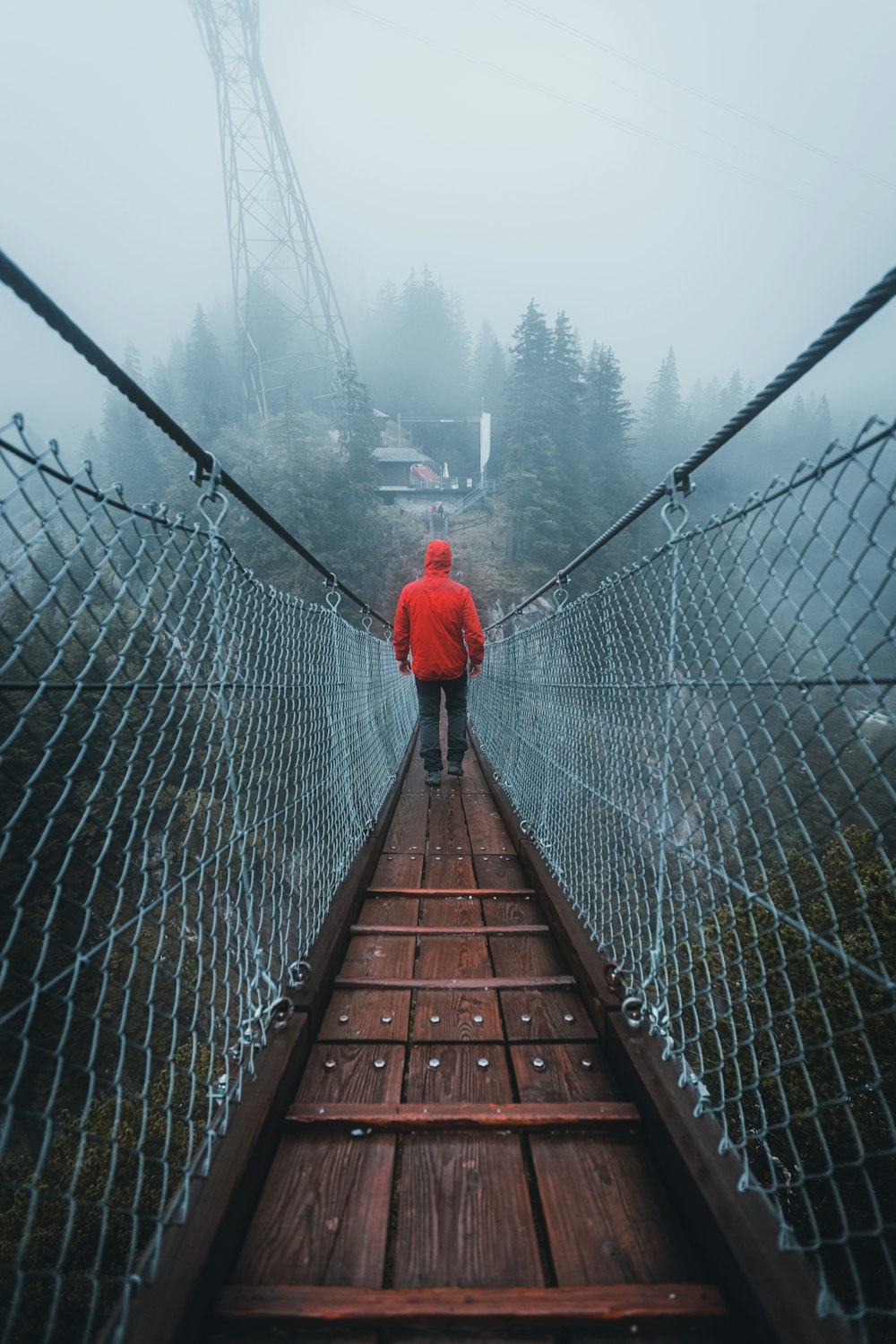 person in red hoodie walking on brown wooden bridge during daytime