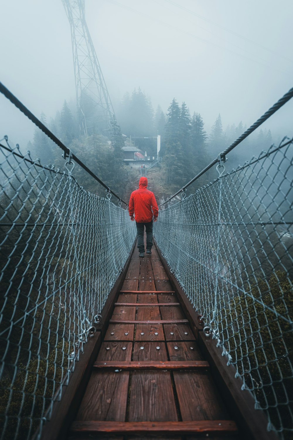 persona in felpa con cappuccio rossa che cammina sul ponte di legno marrone durante il giorno