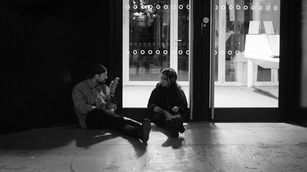 man and woman sitting on floor in grayscale photography