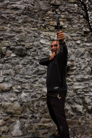 An archer drawing a bowstring back on a sunny outdoor range, muscles tense with concentration.