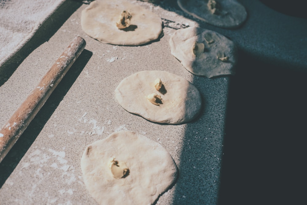 four uncooked pizza doughs on a baking sheet