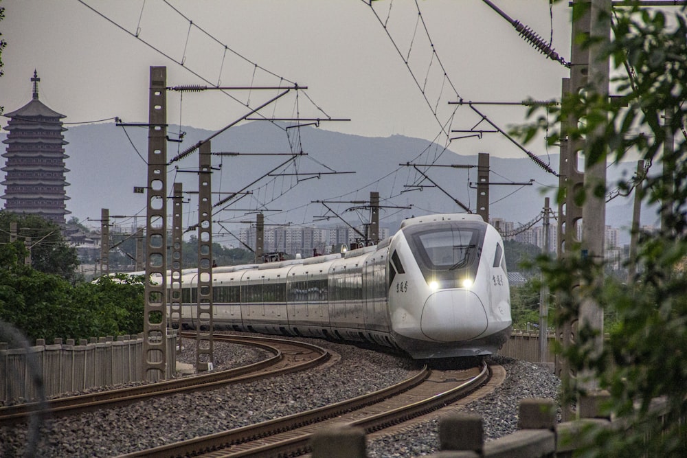 a white train traveling down train tracks next to a forest