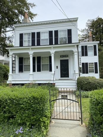Classic colonial residence featuring creamy off-white paint paired with black shutters and a welcoming front porch.