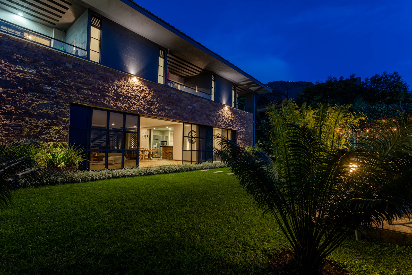 Fachada de casa contemporânea de dois pavimentos com iluminação externa acesa no fim da tarde.