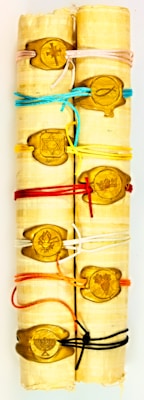 Several scrolls are tightly wrapped together with various colored strings. Each string is held in place by a wooden seal featuring different symbols such as a cross, fish, Star of David, and other icons.