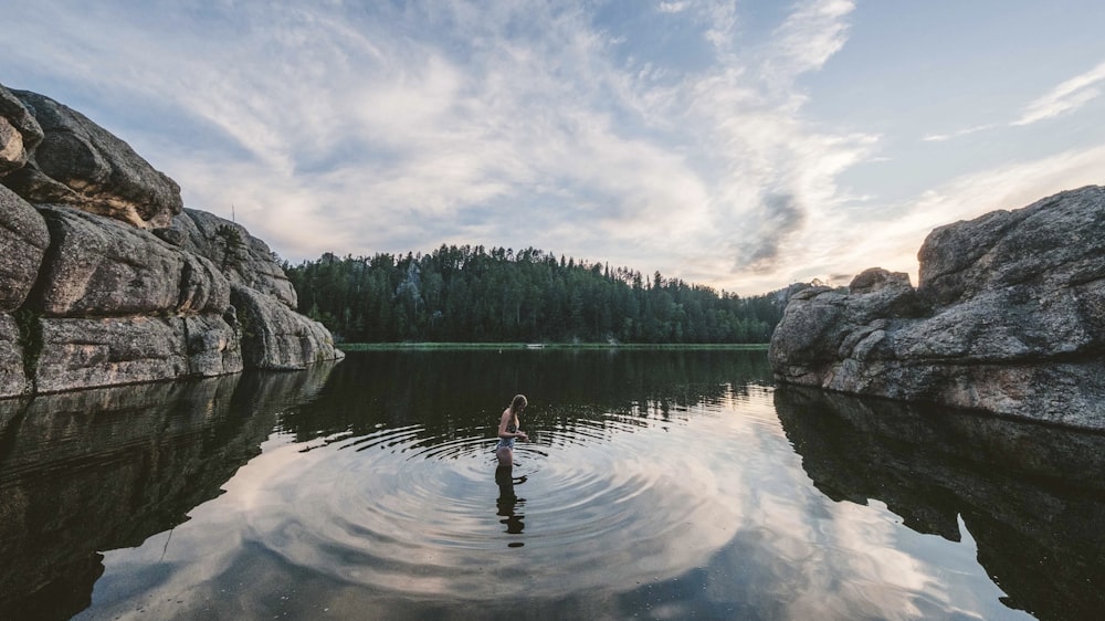 a person standing in a lake surrounded by rocks