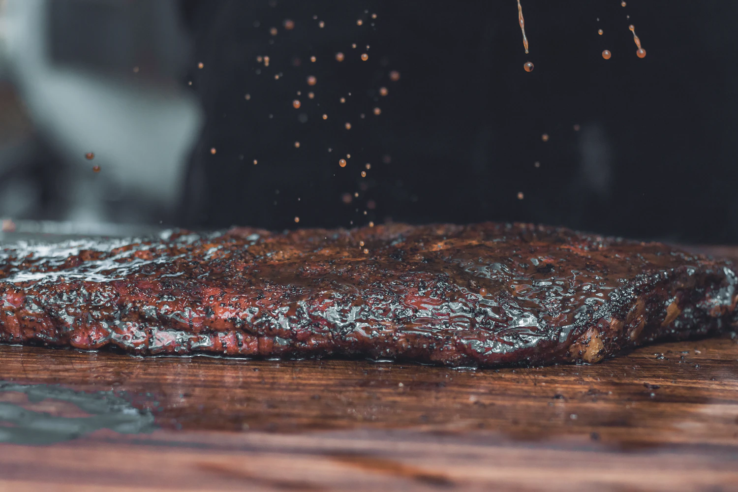 Dry rub falling in a cloud of flecks onto a bark-crusted brisket