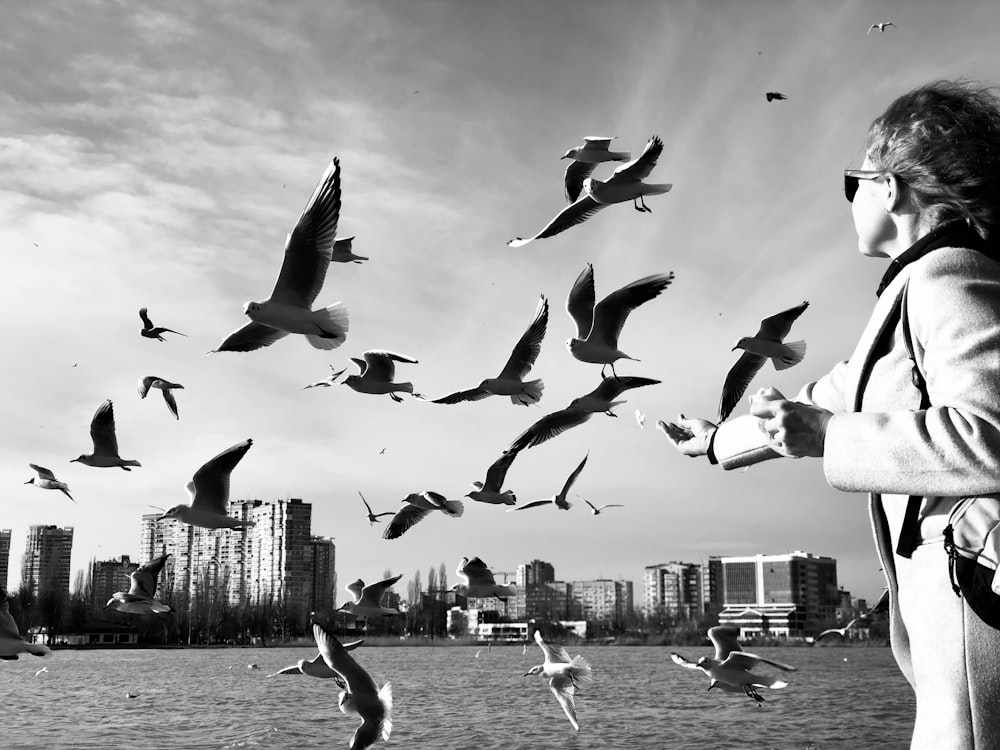 a black and white photo of a woman feeding seagulls