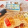 A table covered with a checkered cloth displays a paperback book titled 'All the Bright Places' alongside a deck of Monopoly Deal cards. Nearby, there's a black portable speaker and a pair of sunglasses resting on the table.