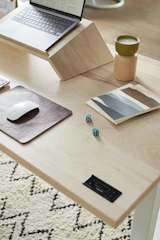 A sunlit desk with a flickering candle, open book, salt lamp, and laptop showing a minimalist calendar wallpaper.